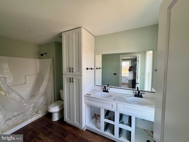 full bath with double vanity, a sink, toilet, and wood finished floors