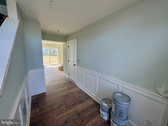 hall with dark wood-style flooring, a wainscoted wall, and a decorative wall