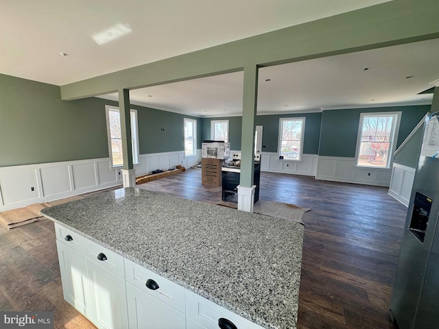 kitchen with light stone counters, a wealth of natural light, open floor plan, and a wainscoted wall