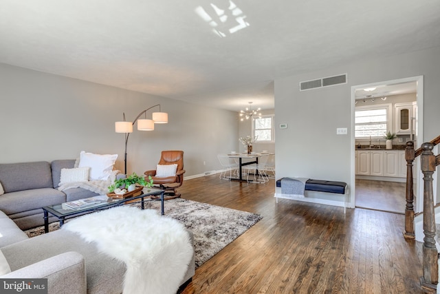 living area featuring visible vents, baseboards, dark wood-type flooring, and a notable chandelier