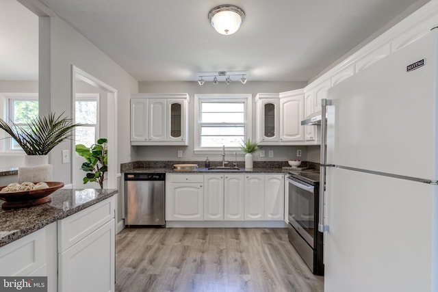 kitchen with a sink, white cabinetry, appliances with stainless steel finishes, glass insert cabinets, and a healthy amount of sunlight