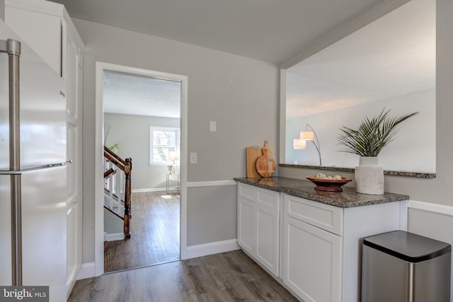 kitchen with wood finished floors, freestanding refrigerator, dark stone counters, white cabinets, and baseboards