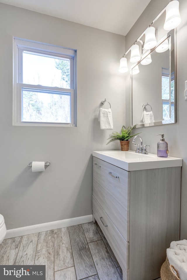 bathroom with toilet, vanity, baseboards, and wood finished floors