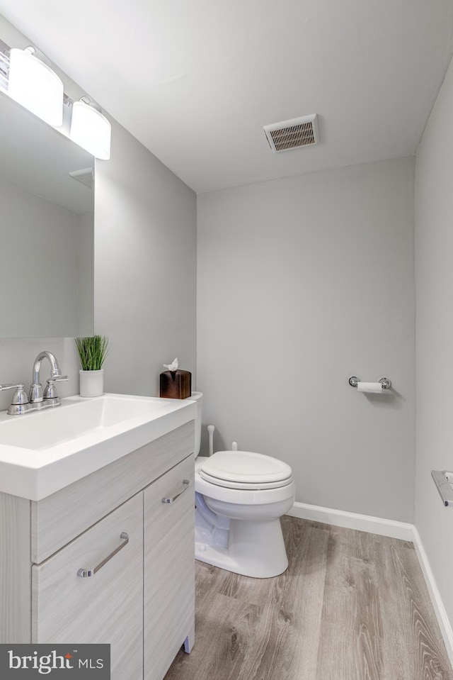 bathroom featuring vanity, wood finished floors, visible vents, baseboards, and toilet