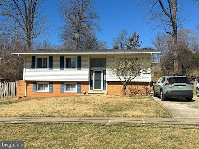 raised ranch with a front yard, fence, and brick siding