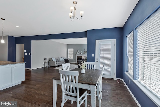 dining area with a chandelier, a fireplace, baseboards, and dark wood-style floors