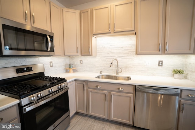 kitchen with gray cabinetry, a sink, backsplash, appliances with stainless steel finishes, and light countertops