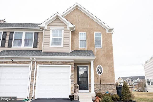 townhome / multi-family property featuring roof with shingles, stucco siding, driveway, stone siding, and an attached garage