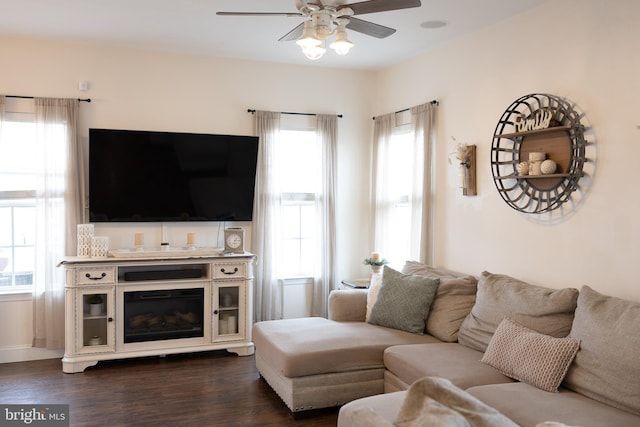 living area featuring a glass covered fireplace, dark wood-style floors, and a ceiling fan