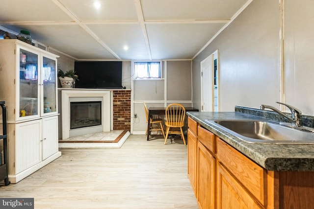 kitchen featuring light wood finished floors, a glass covered fireplace, dark countertops, and a sink