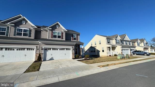 view of property featuring stone siding, a garage, a residential view, and driveway