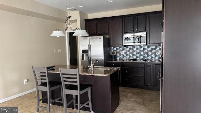 kitchen featuring a kitchen island with sink, a sink, stone countertops, appliances with stainless steel finishes, and decorative backsplash