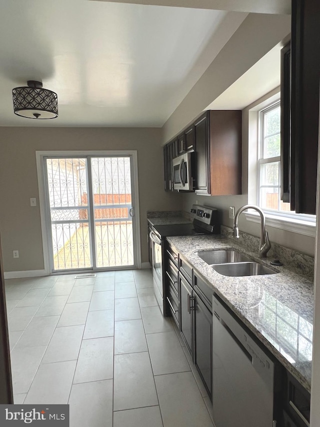 kitchen with baseboards, light stone counters, light tile patterned floors, stainless steel appliances, and a sink
