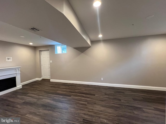 below grade area with dark wood-type flooring, baseboards, recessed lighting, and a fireplace