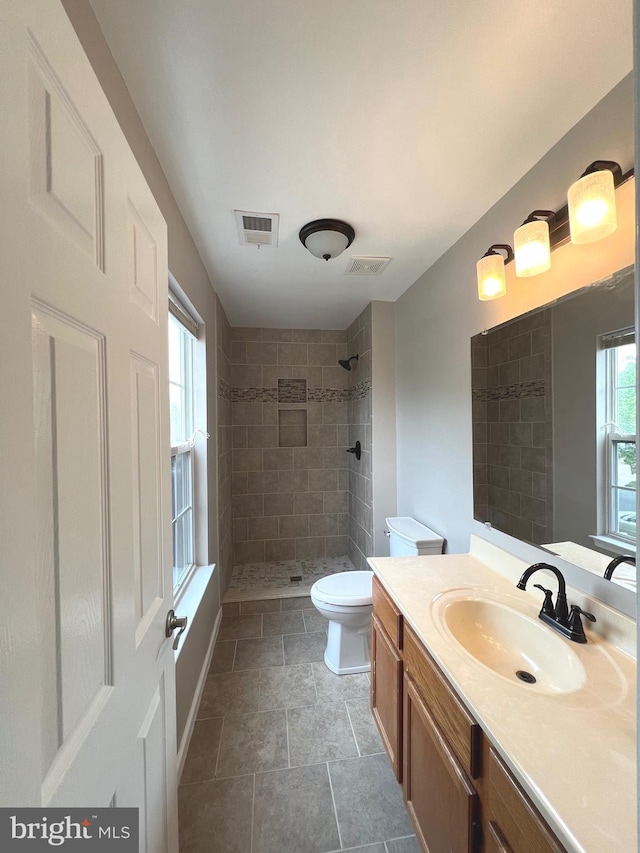 full bath featuring vanity, visible vents, a tile shower, and toilet