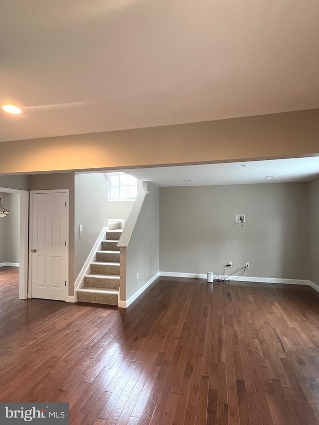 below grade area with dark wood-type flooring, baseboards, recessed lighting, and stairs