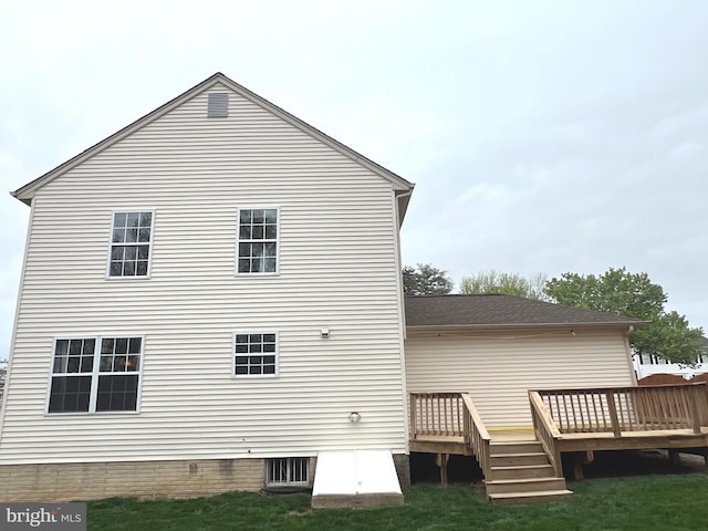 back of house with roof with shingles, a wooden deck, and a lawn