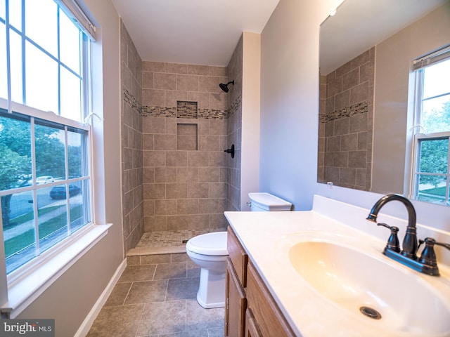 full bath with toilet, tiled shower, vanity, and baseboards