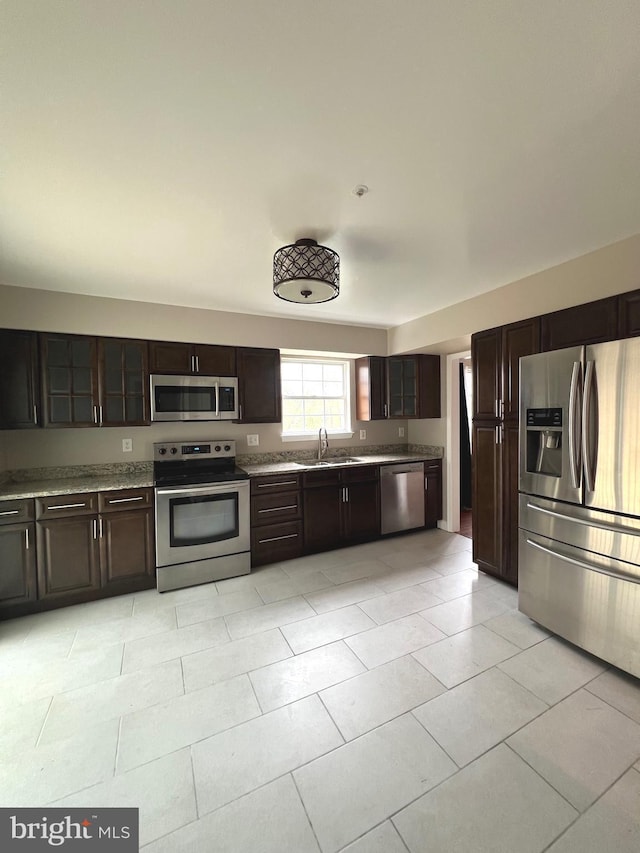 kitchen featuring stainless steel appliances, dark brown cabinetry, a sink, and light tile patterned flooring