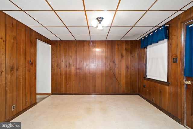 spare room featuring light floors, baseboards, wood walls, and a paneled ceiling