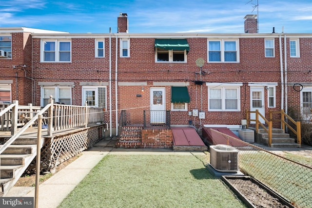 rear view of house featuring a yard, central AC unit, brick siding, and a chimney