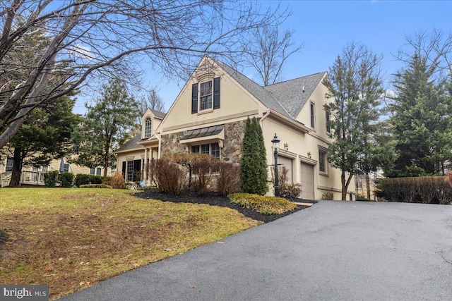 view of side of property with a yard, stucco siding, an attached garage, stone siding, and driveway