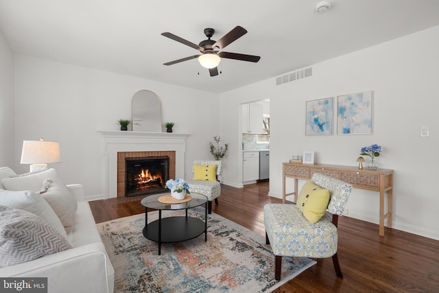 living area with a ceiling fan, baseboards, wood finished floors, visible vents, and a fireplace