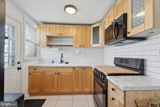 kitchen featuring a sink, gas range oven, black microwave, light tile patterned floors, and light stone countertops