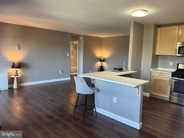 kitchen with a breakfast bar area, dark wood-type flooring, baseboards, light countertops, and appliances with stainless steel finishes