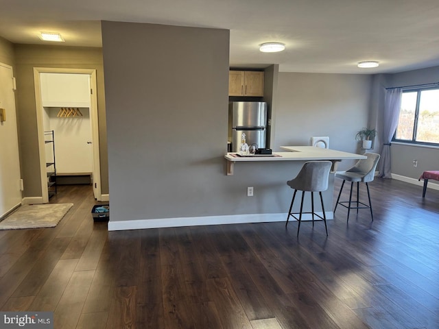 kitchen with baseboards, dark wood-type flooring, freestanding refrigerator, and a kitchen breakfast bar