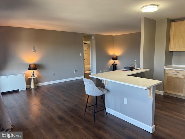 kitchen with dark wood-style floors, a breakfast bar area, light countertops, light brown cabinets, and a peninsula