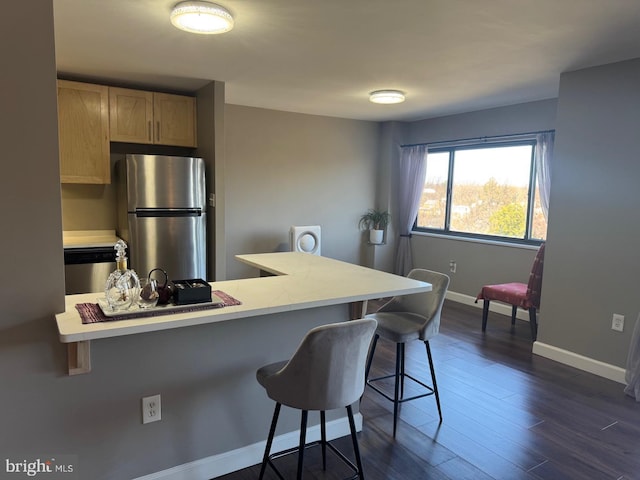 kitchen featuring a breakfast bar area, light countertops, freestanding refrigerator, dark wood-style floors, and light brown cabinetry