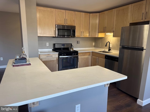 kitchen with appliances with stainless steel finishes, a sink, a peninsula, and light brown cabinetry