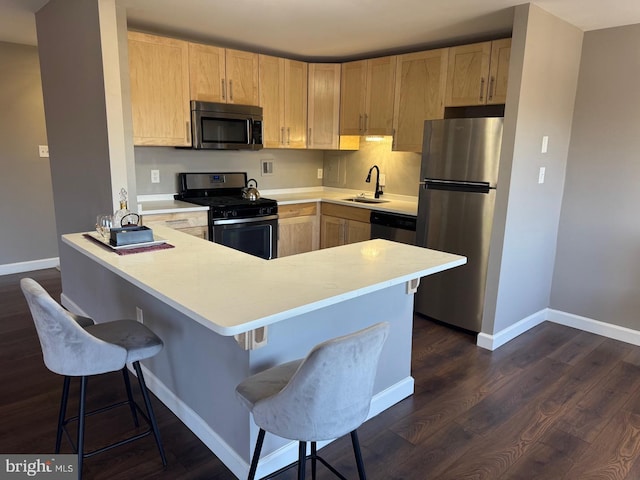 kitchen featuring dark wood-style flooring, stainless steel appliances, light brown cabinets, a sink, and a peninsula