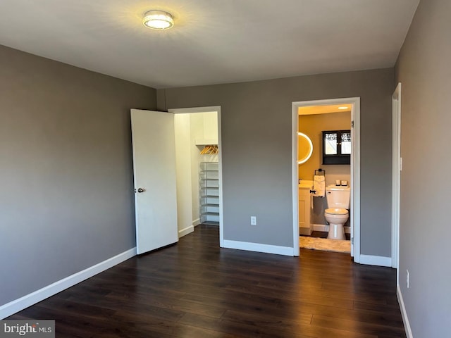 unfurnished bedroom featuring dark wood-style floors, baseboards, and a walk in closet