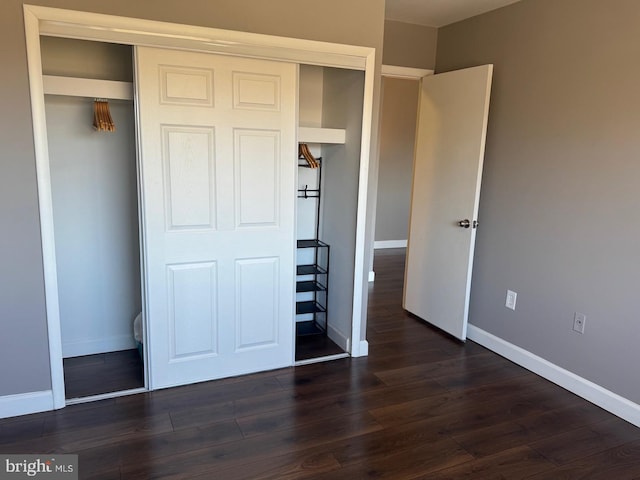 unfurnished bedroom with a closet, dark wood finished floors, and baseboards