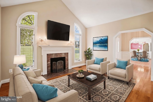 living area with a high end fireplace, high vaulted ceiling, baseboards, and wood finished floors