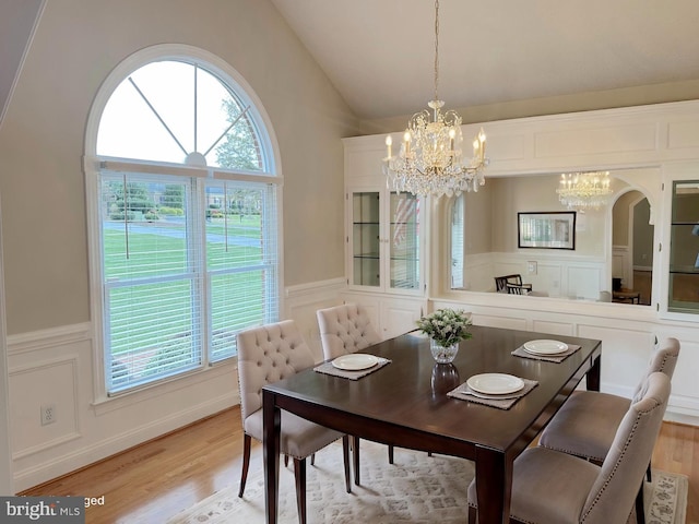 dining room featuring a decorative wall, light wood-style floors, an inviting chandelier, and vaulted ceiling