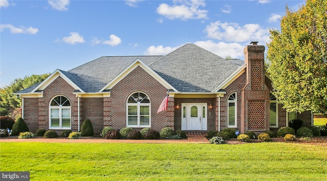 view of front facade with brick siding, a chimney, a front lawn, and roof with shingles