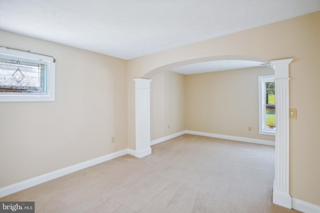 unfurnished room featuring arched walkways, a healthy amount of sunlight, light colored carpet, and decorative columns