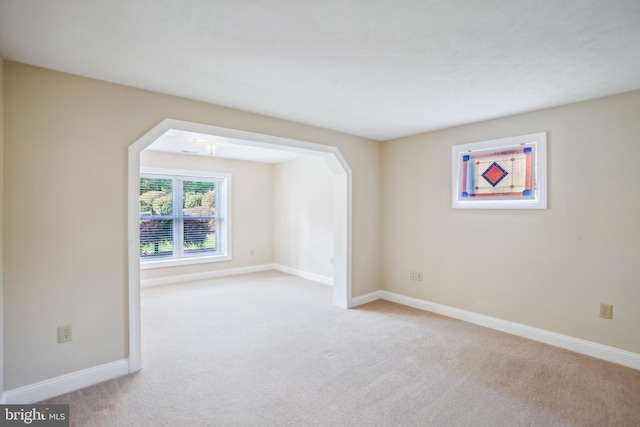 carpeted spare room featuring baseboards and arched walkways