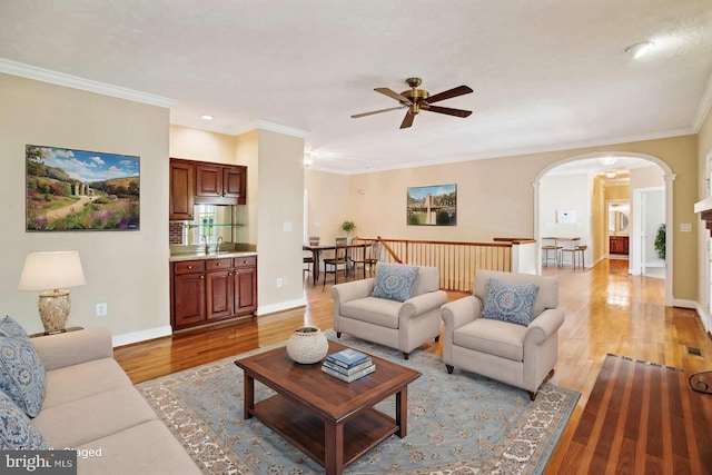 living area with crown molding, a ceiling fan, arched walkways, and light wood finished floors