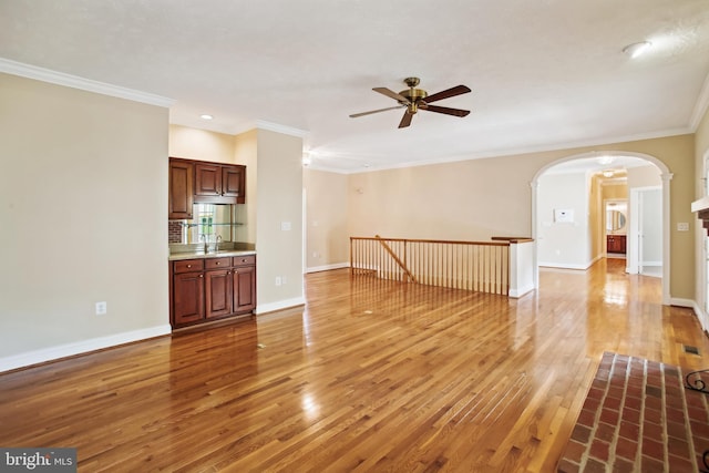 unfurnished living room featuring light wood-style flooring, arched walkways, baseboards, and ceiling fan