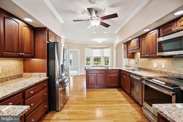 kitchen featuring a peninsula, light wood-style flooring, a sink, ornamental molding, and stainless steel appliances