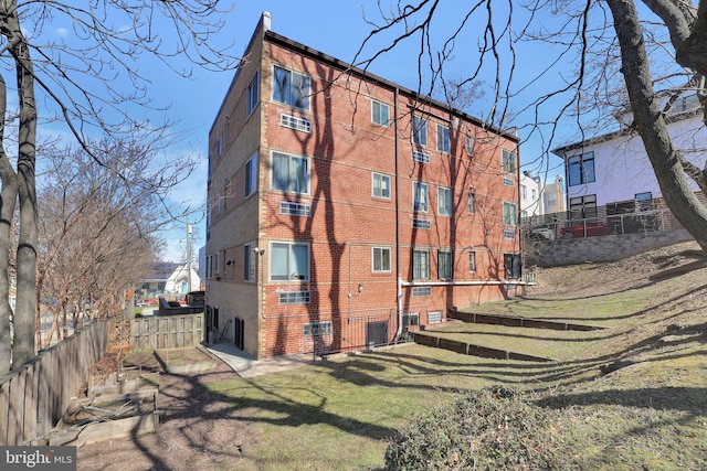 rear view of property featuring brick siding, a lawn, central AC unit, and fence