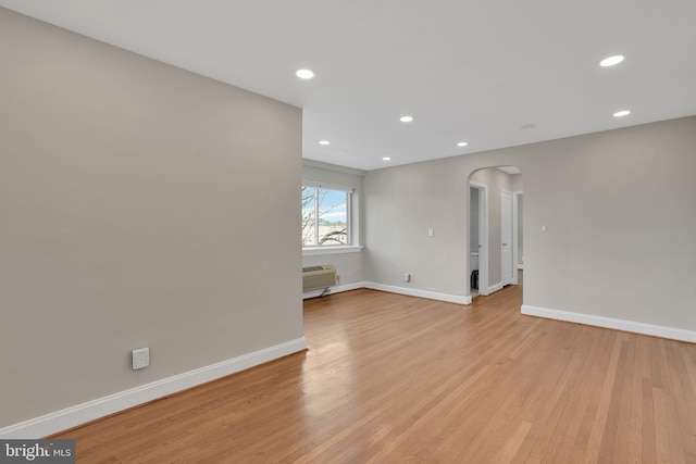 empty room featuring light wood-style floors, arched walkways, and baseboards