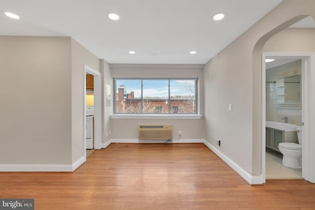 empty room with baseboards, arched walkways, an AC wall unit, light wood-style floors, and recessed lighting