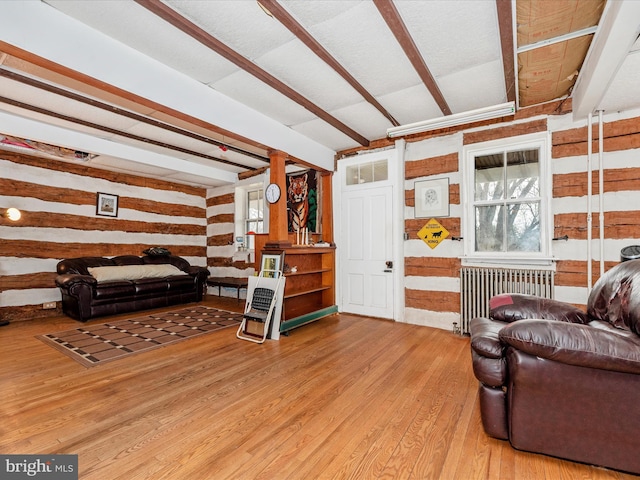 living area with a wealth of natural light, beam ceiling, wood finished floors, radiator heating unit, and wooden walls