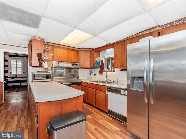 kitchen featuring a drop ceiling, brown cabinets, appliances with stainless steel finishes, light wood-style floors, and a sink