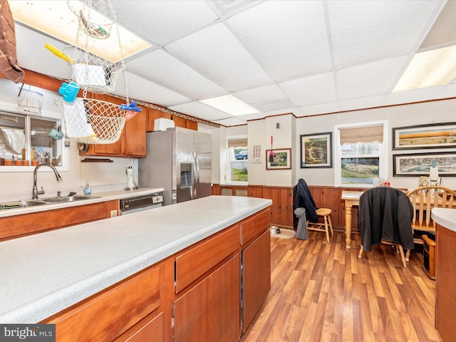 kitchen with a sink, a paneled ceiling, brown cabinets, and stainless steel fridge with ice dispenser